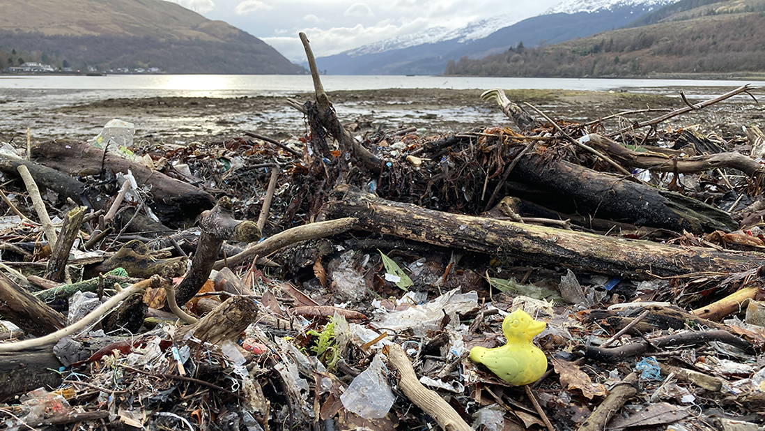 A beach strewn with litter including a yellow plastic duck