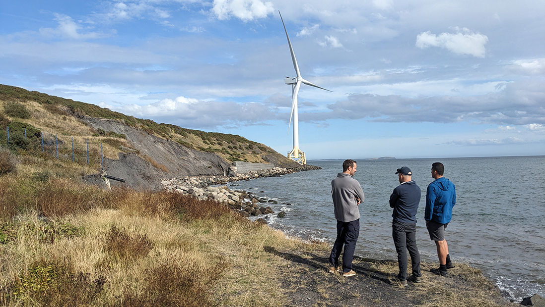 Members of the RACC team on a coastal path with a view of a landfill site and wind turbine