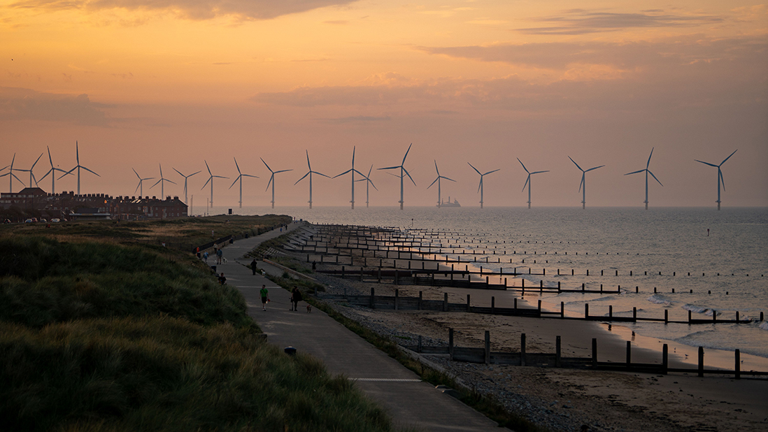 Sunset over the coast with offshore wind turbines in the distance