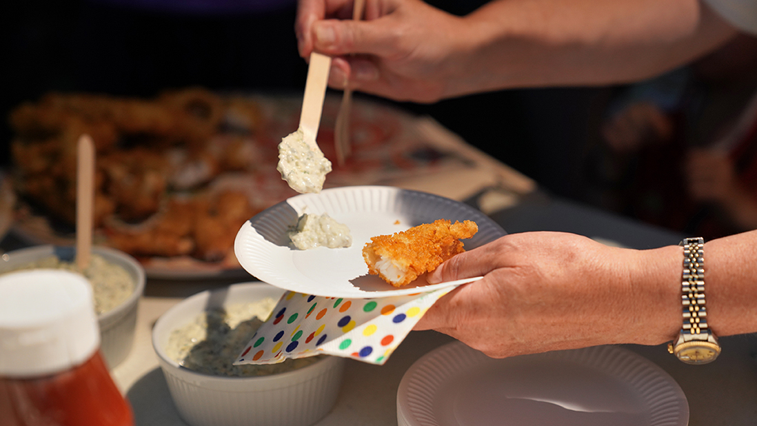 A close-up of a plate with part of a breaded fish portion which is about to be stabbed with a fork