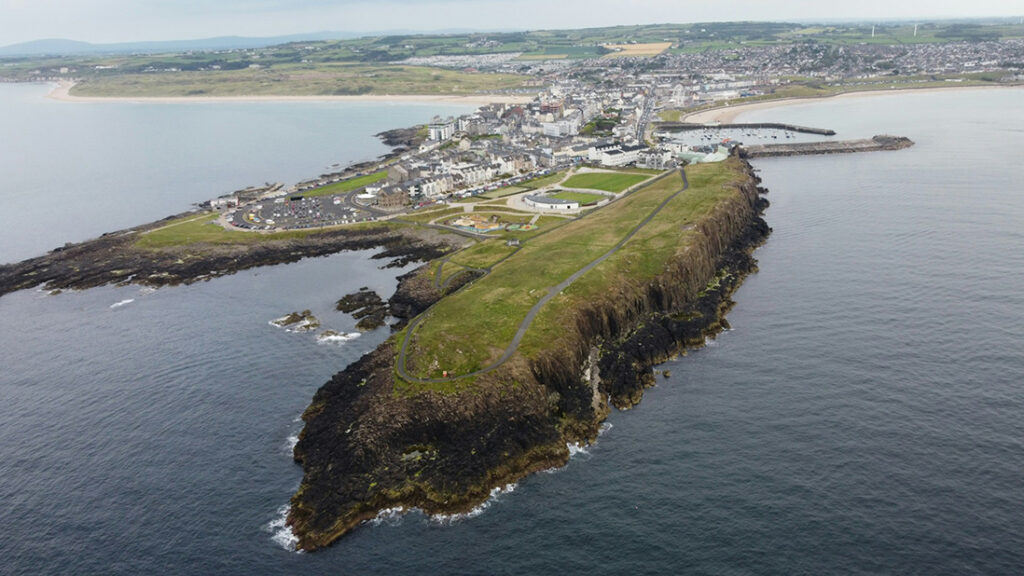 Aerial view of Portrush area showing buildings and a pier on land that juts on into the sea