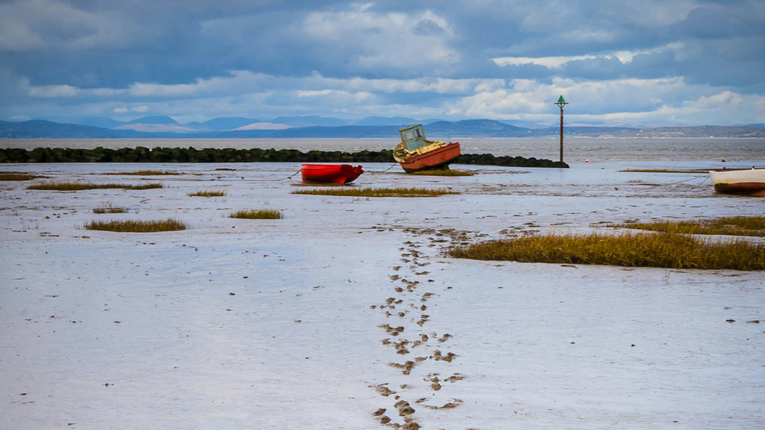 Footprints across muddy sand lead to a small fishing boat and the sea beyond